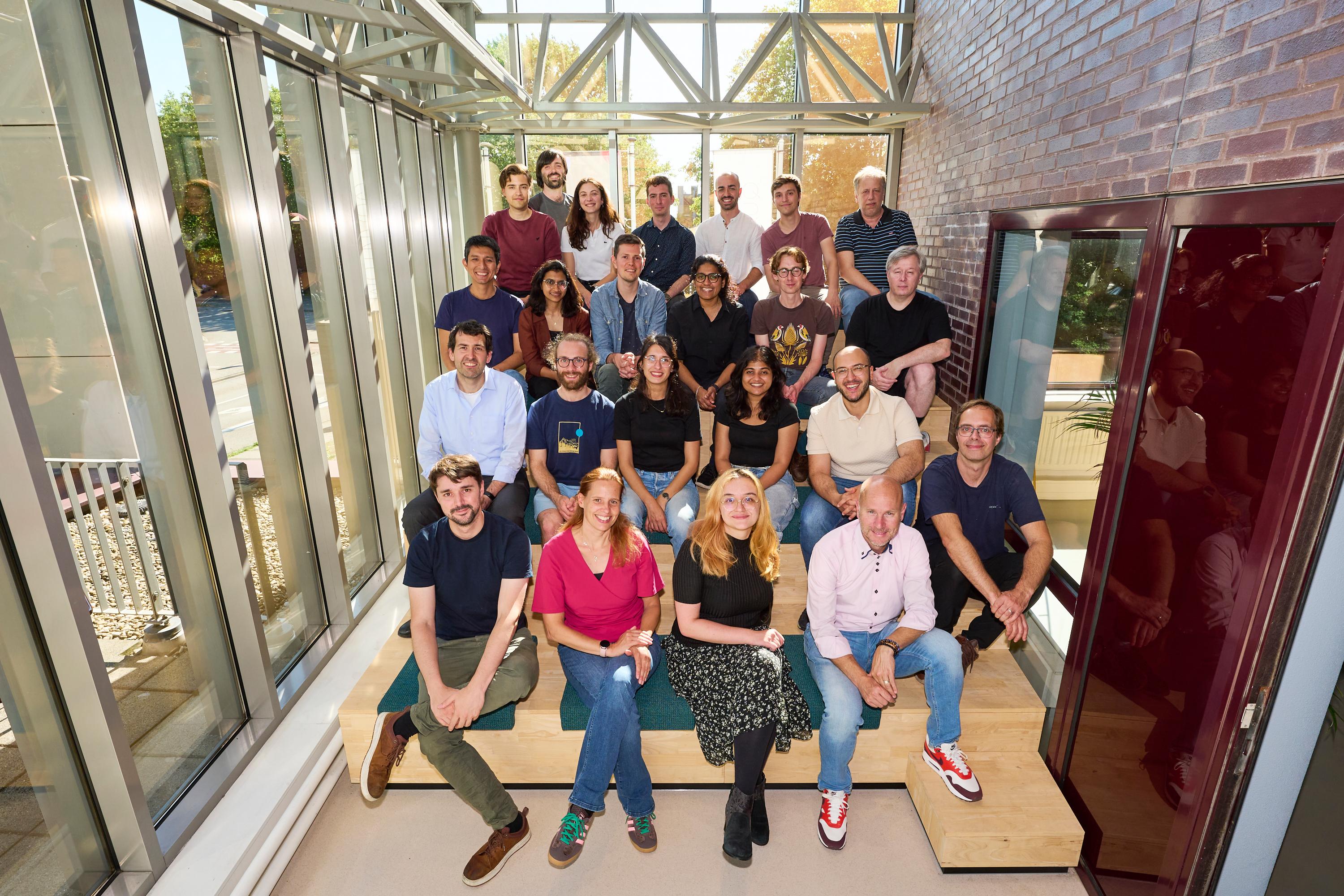 Twenty-three people from the Q*Bird team sit posed in their office space.
